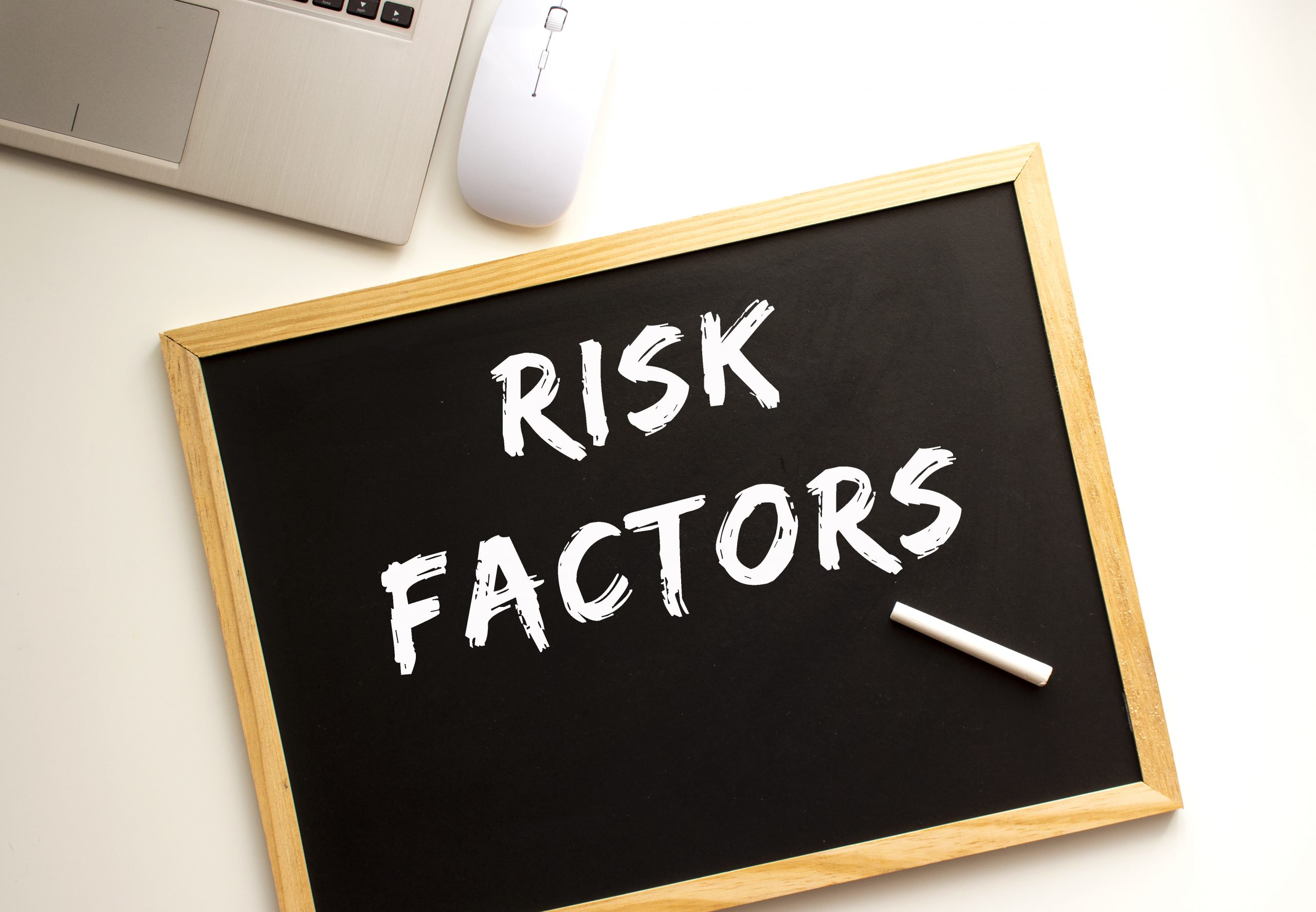 Text RISK FACTORS written in chalk on a slate board. Office desk. Business concept.